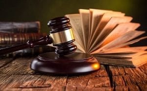 A gavel on a wooden block rests on a desk with legal books in the background. 