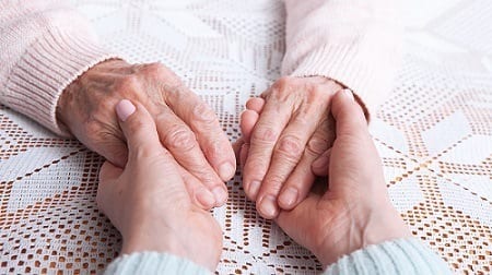 Older hands hold younger hands. Nursing home abuse concept photo.
