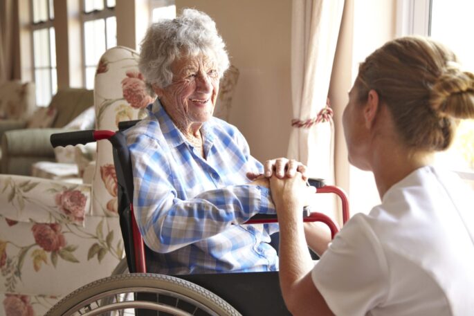 an older woman in a wheelchair smiles at a younger woman