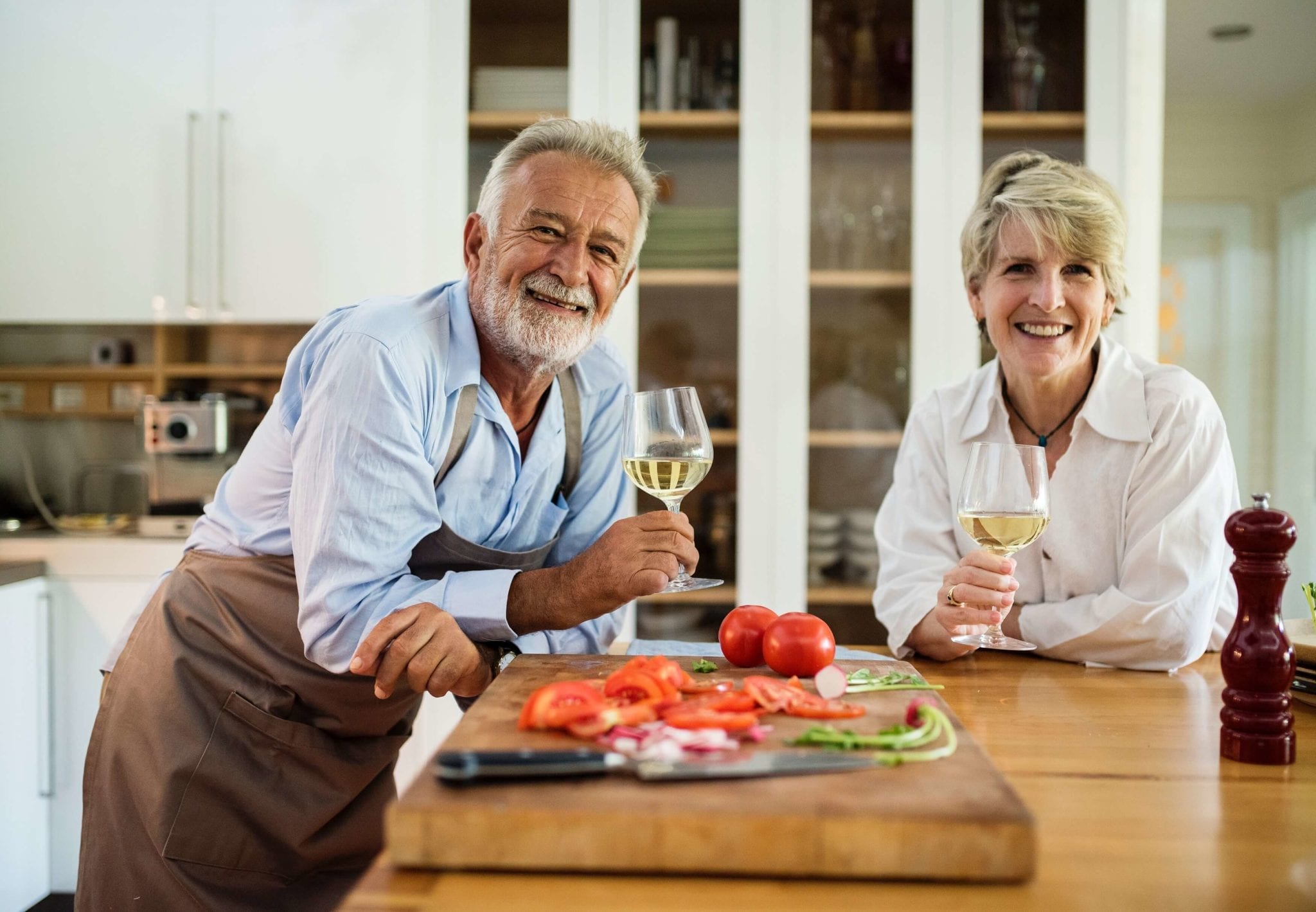 Two older adults enjoy wine and vegetables in their kitchen