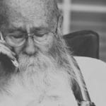An older man with a beard and glasses talks on the phone