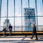 a businessman walks near a large window with a city backdrop