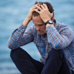 A man sits holding his head in his hands