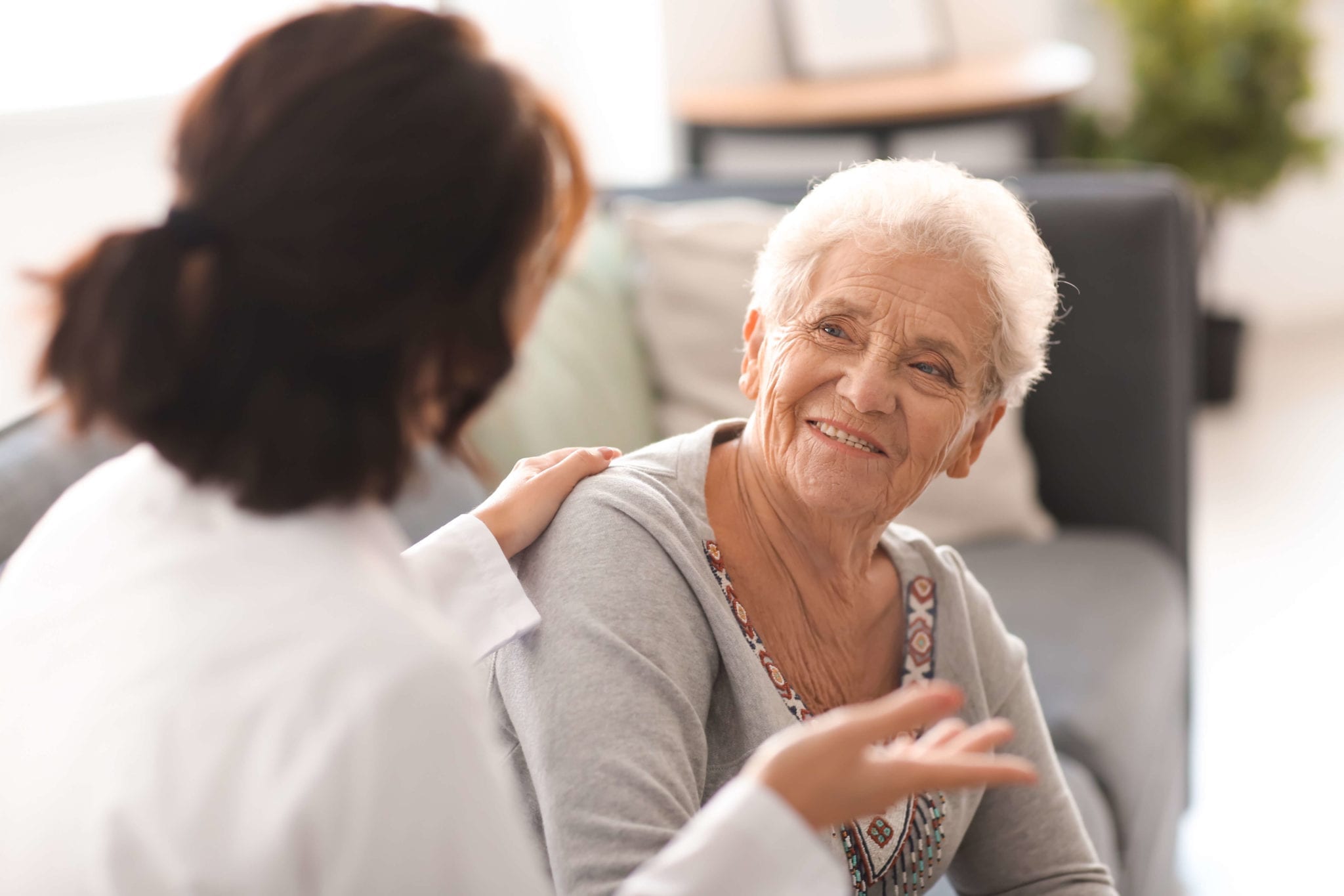 A woman talks to an old lady in a nursing home.