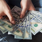 close up of woman holding several $100 bills