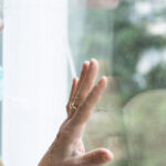 older woman with a mask looking out a window