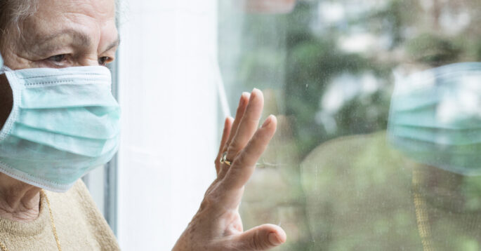older woman with a mask looking out a window