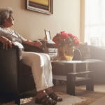 an older woman sits in a chair and looks pensively out a window