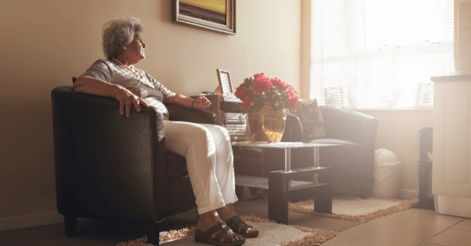 an older woman sits in a chair and looks pensively out a window