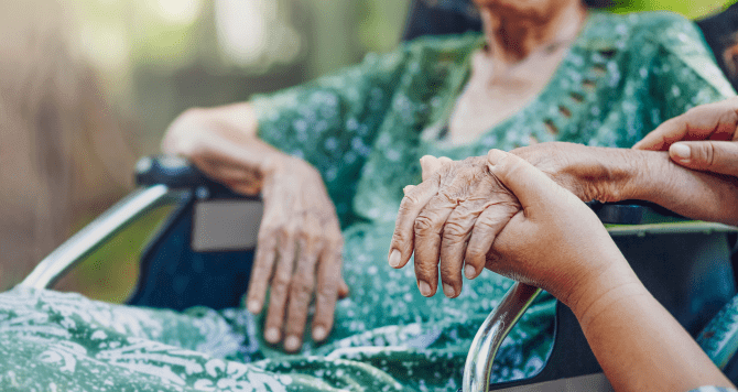 elderly woman in wheelchair holding a loved ones hand
