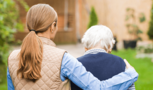 A woman walks outside with an older adult during a visit to a nursing home.
