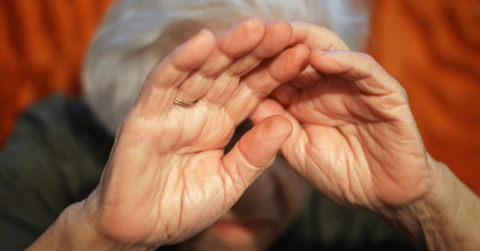 an older woman cowers in fear and covers her face with her hands