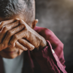 a sad older adult covers his face with his hands
