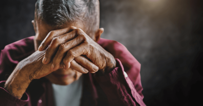 a sad older adult covers his face with his hands