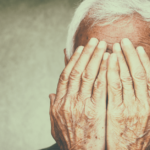 a sad older man with his head in his hands