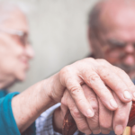 two seniors hold hands over a cane