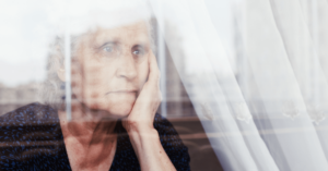 An older woman looking out the window of her nursing home with a sad expression.