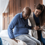 an older man is helped out of bed by a nurse