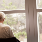 Elderly person sits alone looking out window