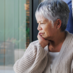Woman sits with hand on chin while looking out a window