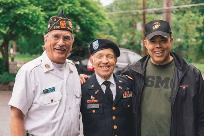 Three older male veterans smile together outside