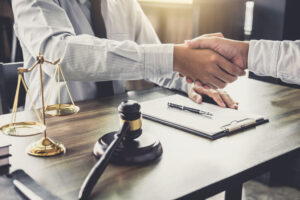 Two attorneys shaking hands during a nursing home lawsuit meeting, with a gavel and scales of justice on the desk.