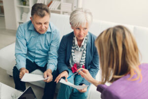 A couple sits on a couch, holding papers, discussing options with a nursing home lawyer.