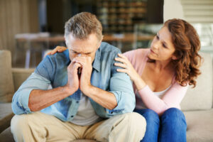 A man sits with his head in his hands, visibly distressed, while a woman beside him offers comfort and support.