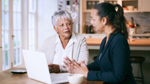 An older woman and an attorney sitting at a kitchen table with a laptop, discussing a nursing home lawsuit.