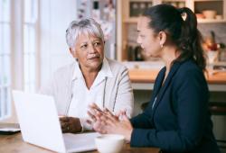 An attorney speaks with an older adult at a table with a laptop.
